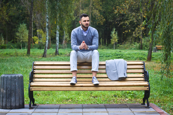 Young sexy guy sitting on a bench in an autumnal, summer park. A man contemplating new ideas while walking. European countryside. Stock Photo - Fotó, kép