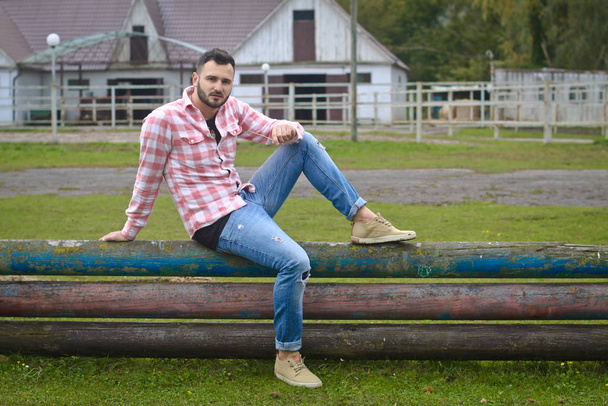 Young handsome guy Cowboy. male farmer is sitting on his fence on his ranch. Rural landscapes, countryside. Trees, field, farm. Stock photos for desig - Foto, Bild