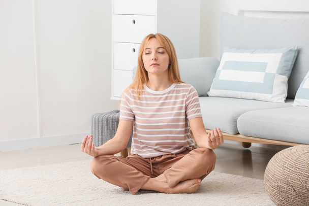 Beautiful mature woman meditating at home - Фото, зображення