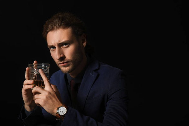 Porträt eines gutaussehenden Geschäftsmannes mit einem Glas Alkohol auf dunklem Hintergrund - Foto, Bild