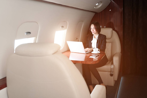 Üzletasszony laptoppal a fedélzetén a modern magánrepülőgép - Fotó, kép