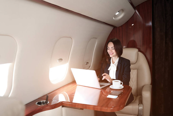 Zakenvrouw met laptop aan boord van het moderne privévliegtuig - Foto, afbeelding