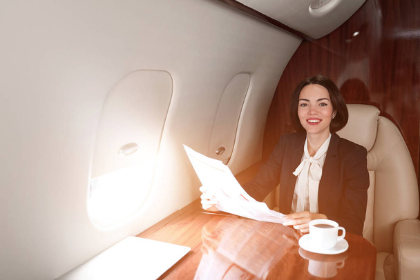 Bizneswoman czytanie gazety na pokładzie nowoczesnego samolotu prywatnego - Zdjęcie, obraz