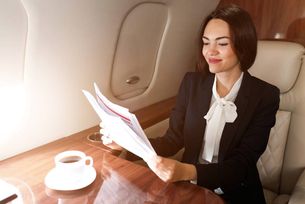Geschäftsfrau liest Zeitung an Bord des modernen Privatflugzeugs - Foto, Bild