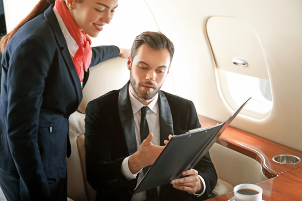 Хозяйка самолета показывает бизнесмену меню на борту современного частного самолета
 - Фото, изображение