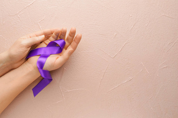 Női kéz lila szalaggal, mint szimbólum a rák világnapja színes háttér - Fotó, kép