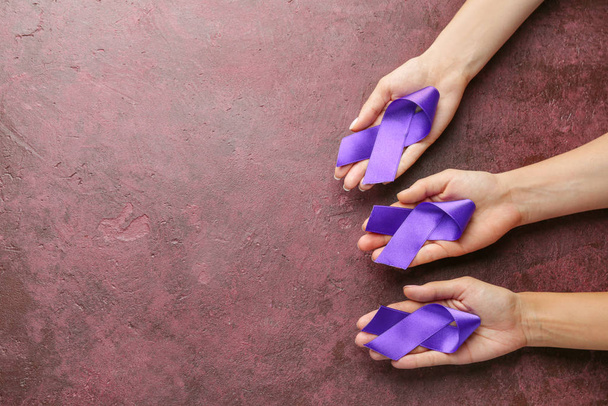Female hands with purple ribbons as symbol of World Cancer Day on color background - Foto, Bild