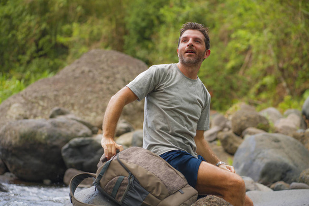 young happy and attractive man with travel backpack hiking in river at forest feeling free enjoying nature and fresh environment on summer trekking journey - Φωτογραφία, εικόνα