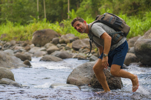 young happy and attractive man with travel backpack hiking in river at forest feeling free enjoying nature and fresh environment on summer trekking journey - Valokuva, kuva