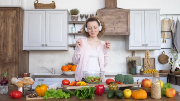 Beautiful Pregnant Woman Preparing Meal And Dancing In Headphones On Kitchen. - Materiał filmowy, wideo