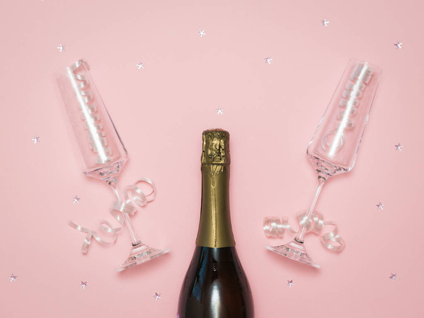 Two crystal champagne glasses on a festive pink background with a bottle of champagne. - Fotoğraf, Görsel