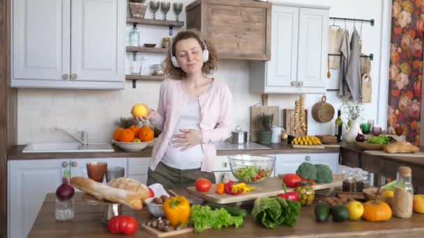 Pregnant Woman Wearing Headphones And Dancing With Apple On Kitchen. - Filmagem, Vídeo