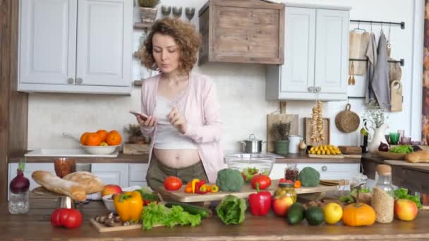 若い妊娠中の女性は、スマートフォンでレシピを探しているとキッチンでサラダを作る. - 映像、動画