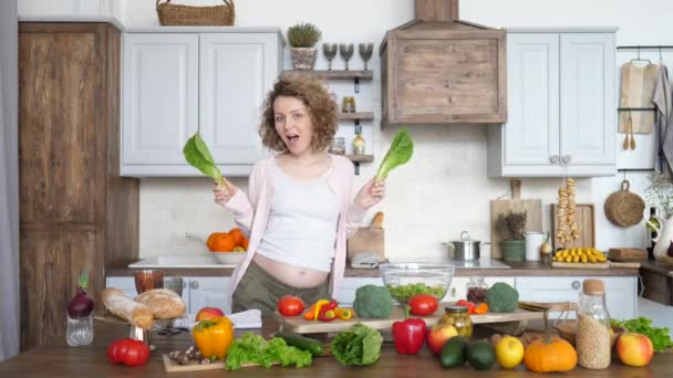 Счастливая беременность женщины, танцующей с зеленым салатом на кухне
 - Кадры, видео