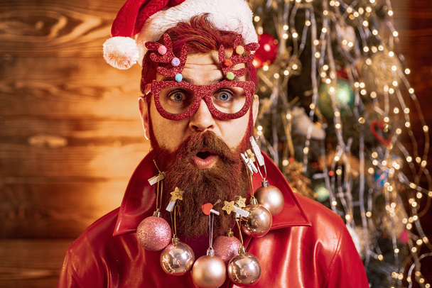 Красивый мужчина в рождественском платье. Санта позирует на старинном деревянном фоне. Новогодние праздники
. - Фото, изображение