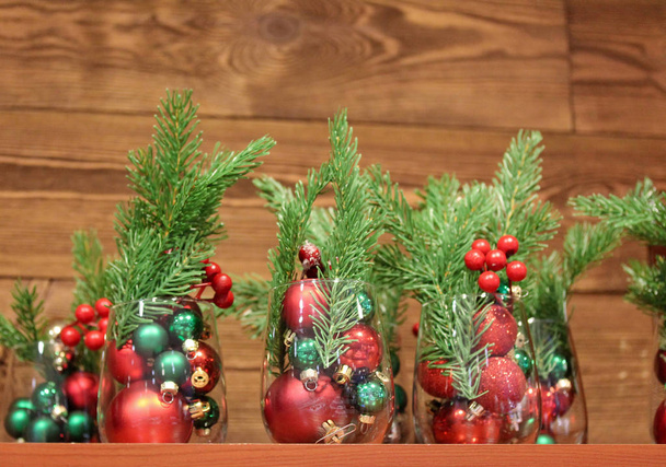 Christmas baubles in high glasses with fir branches and holly berries - Photo, Image