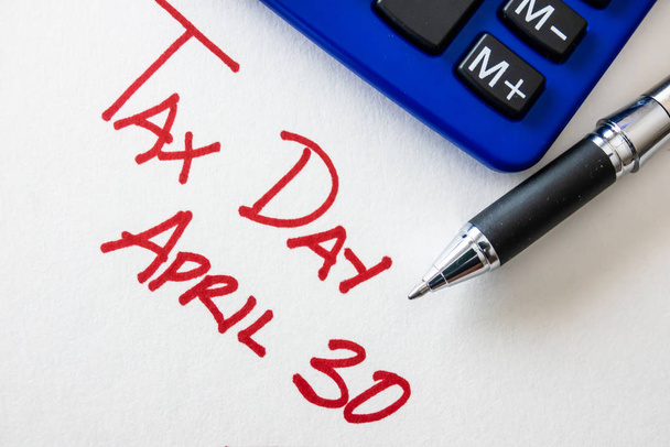 Calculator met pen op witte achtergrond met Tax day sign op de voorgrond - Foto, afbeelding