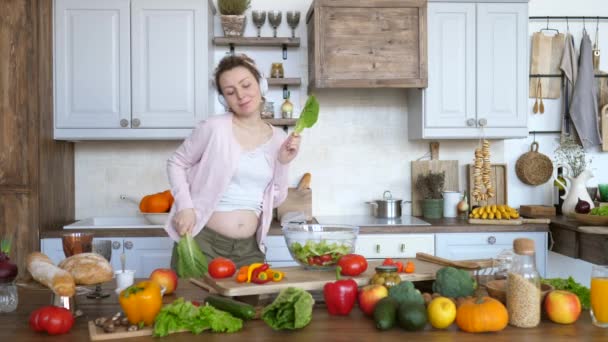 Happy Pregnant Woman Dancing With Green Salad Leaves In Kitchen While Cooking. - Video, Çekim