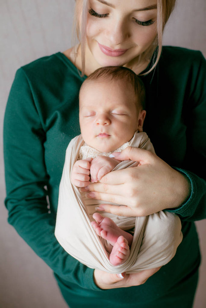 Beautiful young mother with blond hair and in a green dress holds a baby in her arms at home. Happy motherhood - Photo, image