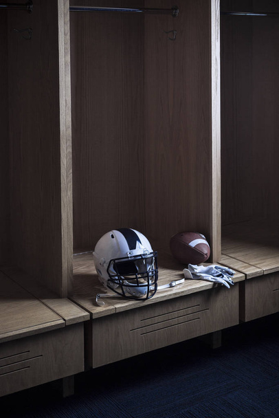 Voetbal en een helm in de kleedkamer in een sportstadion. Spotlight toont de individuele locker klaar voor game dag. - Foto, afbeelding