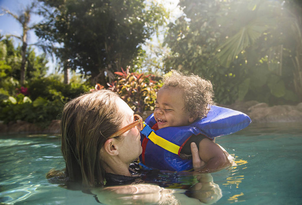 Cute métis petit garçon jouant avec sa mère à une station balnéaire tropicale. S'amuser ensemble dans une belle piscine extérieure. Petit enfant à l'expression heureuse - Photo, image