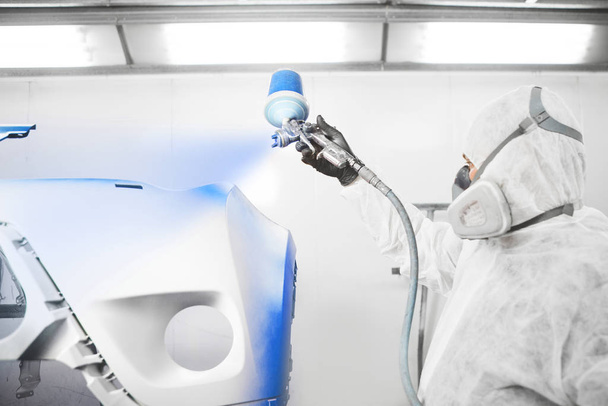 Male worker painting a car bumper in a white paint booth. - Fotografie, Obrázek
