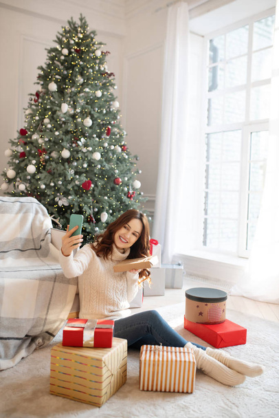 Dark-haired woman sitting on the floor with christmas gifts - Foto, afbeelding