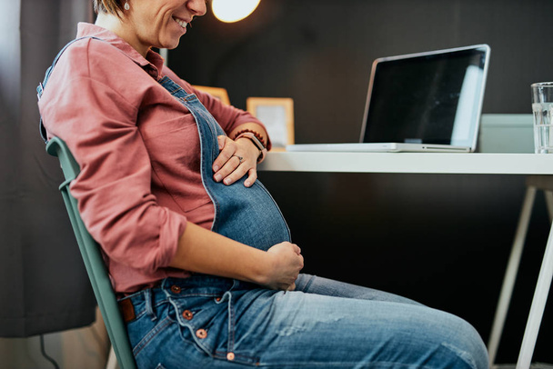 Proud future mother sitting in her home office and touching belly. - Φωτογραφία, εικόνα