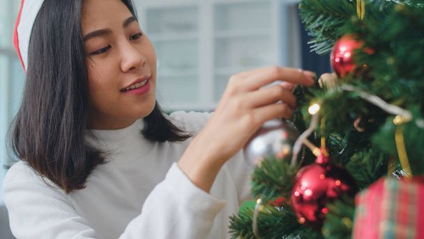 アジアの女性はクリスマスフェスティバルでクリスマスツリーを飾ります。女性の十代の幸せな笑顔は、自宅のリビングルームでxmas冬の休日を祝います。クローズアップショット. - 写真・画像