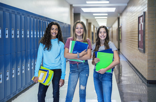 Ομάδα μαθητών Γυμνασίου στέκονται μαζί στο διάδρομο του σχολείου. Γυναίκες συμμαθήτριες χαμογελούν και διασκεδάζουν μαζί κατά τη διάρκεια ενός διαλείμματος στο σχολείο - Φωτογραφία, εικόνα