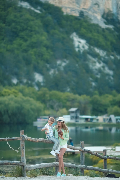 Mom and son near a wooden homemade village fence on the background of the lake - Foto, imagen