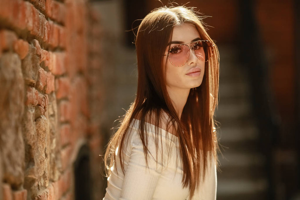 stylish woman in glasses young model in an urban area of the city near the brick walls - Фото, изображение