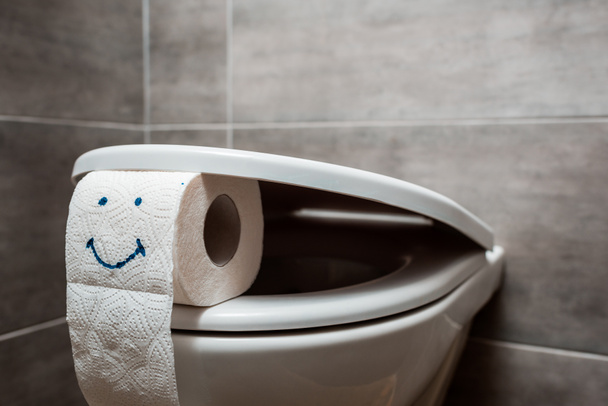 close up view of ceramic clean toilet bowl and toilet paper with smiley face in modern restroom - Zdjęcie, obraz