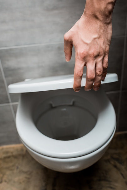 cropped view of man holding toilet lid in modern restroom with grey tile - Fotoğraf, Görsel