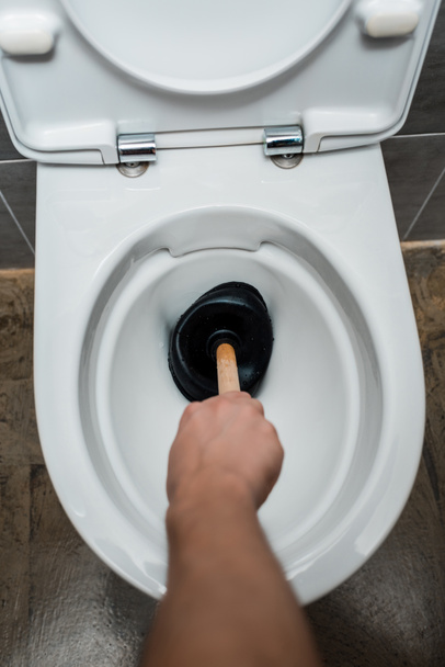 cropped view of plumber using plunger in toilet bowl in modern restroom with grey tile - Foto, immagini