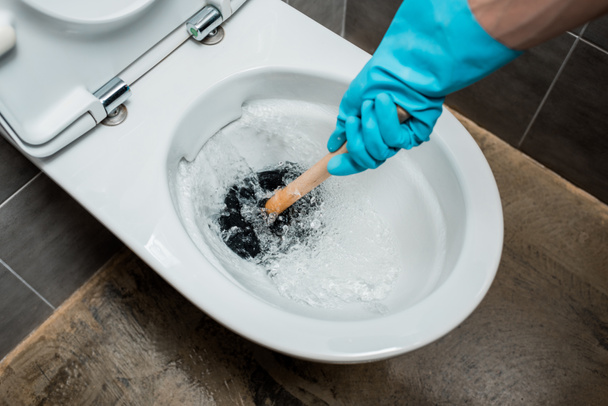 vista ritagliata dell'idraulico usando lo stantuffo nella tazza del water durante lo scarico nel bagno moderno con piastrelle grigie
 - Foto, immagini
