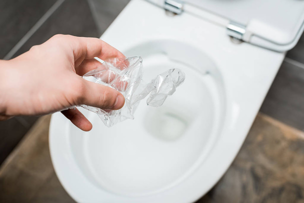 обрізаний вид людини, що кидає зім'яту пластикову пляшку в унітаз в сучасній туалетній кімнаті з сірою плиткою
 - Фото, зображення