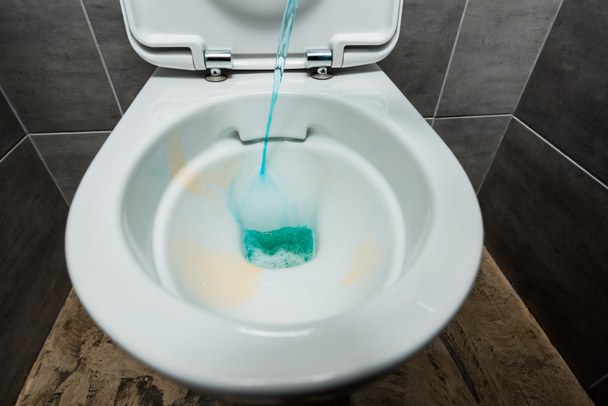 Modern tuvaletteki seramik temiz klozete gri fayanslı mavi sıvı deterjan dökülüyor. - Fotoğraf, Görsel