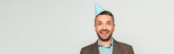 panoramic shot of happy man in party cap looking at camera isolated on grey - Foto, Bild