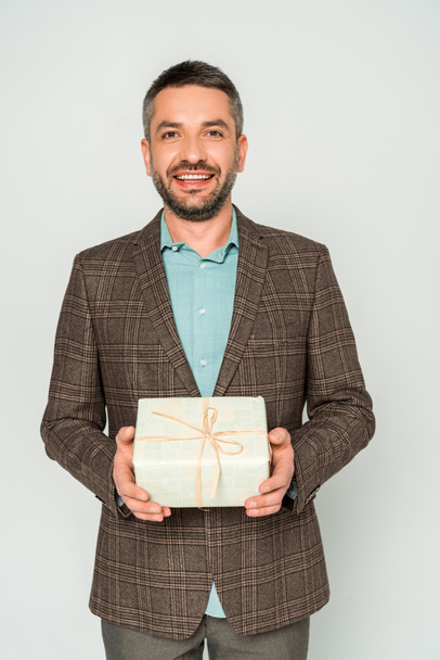 hombre feliz sosteniendo caja de regalo mientras mira la cámara aislada en gris
 - Foto, Imagen