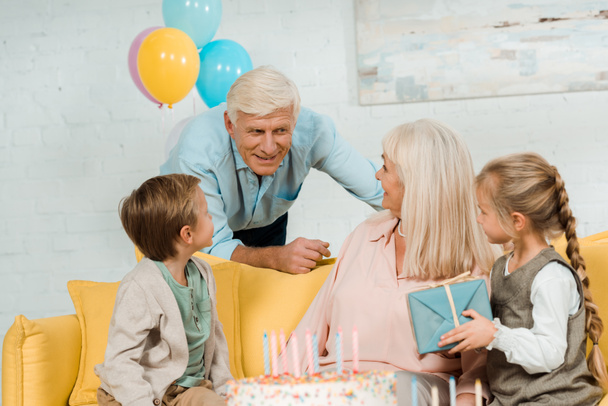 smiling senior man talking to happy wife sitting on sofa with grandchildren - Fotoğraf, Görsel