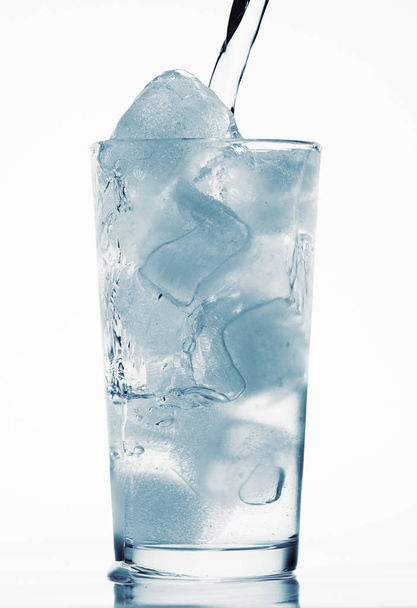 pouring water in a glass full of ice cubes, white background, blue toned object - 写真・画像