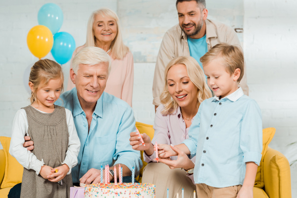 Doğum günü pastasının yanında mumları tutan gülümseyen anne ve oğul ve etrafında duran aile. - Fotoğraf, Görsel