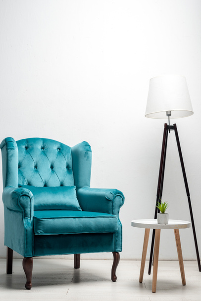 elegant velour blue armchair with pillow near coffee table and floor lamp - Photo, Image