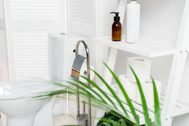 інтер'єр білої сучасної ванної кімнати з унітазом біля розкладного екрану, стійки і пальми
 - Фото, зображення