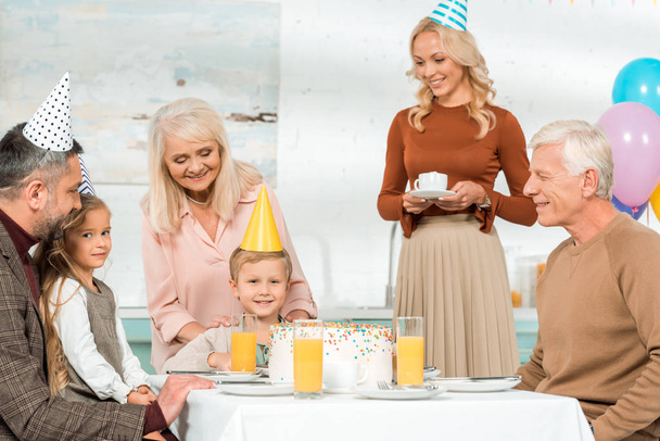 happy family sitting at served kitchen table with birthday cake - Photo, Image