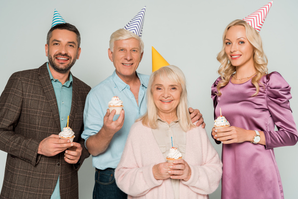 padres ancianos felices con niños adultos sosteniendo cupcakes de cumpleaños aislados en gris
 - Foto, Imagen