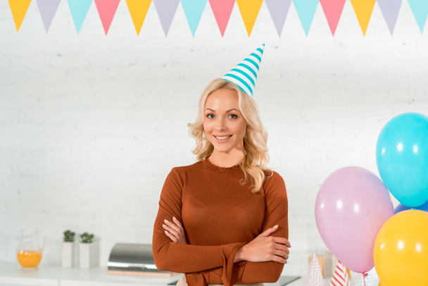 happy woman in party cap standing with crossed arms and smiling at camera - Photo, Image