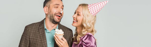 onnellinen nainen tilalla syntymäpäivä cupcake lähellä iloinen aviomies kermavaahtoa nenä eristetty harmaa
 - Valokuva, kuva