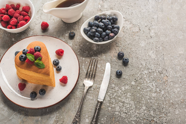 top view of heart shaped pancakes with berries on grey concrete surface with cutlery, maple syrup - Fotografie, Obrázek
